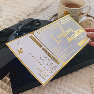 May include: A gold boarding pass with the text "Boarding Pass Happy Mother's Day London" and "Passenger: MUMMA Departure: 11TH AUG 2022 From: ABERDEEN Duration: 2 NIGHTS Booking Ref: MOTHERSDAY 1176 186 187" The boarding pass is in a black box with a black ribbon.
