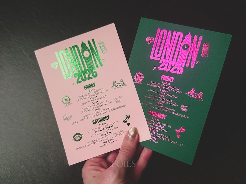 May include: Two event itinerary cards, one pink and one green, with metallic foil text. The cards read "London 2026" and list activities for Friday and Saturday, including train travel, lunch, and theater.