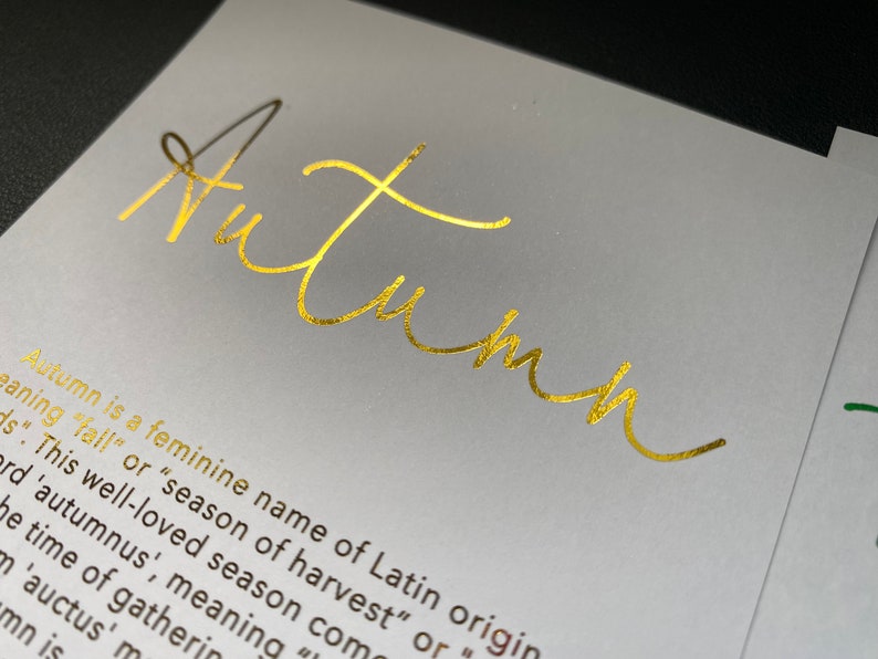 May include: A close-up of a white card with the word "Autumn" in gold script. The card also includes text describing the origin and meaning of the name "Autumn".