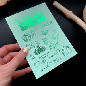 May include: A mint green card with the words "The Exclusive Tour BARCELONA" in shiny green lettering. The card features hand-drawn illustrations of tapas, a sunset, and other Barcelona activities.