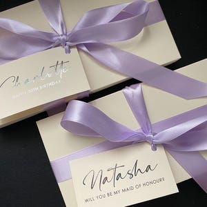 Caja de regalo de lujo color marfil con cinta lila y morada. Etiqueta de nombre personalizada. Regalo de boda o propuesta de dama de honor. Empaque para boletos de licencia de conducir o vales.