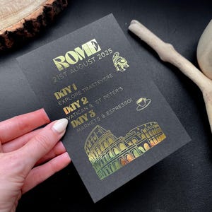 May include: Black card with gold foil text reading "ROME 21ST AUGUST 2025." It lists a 3-day itinerary: Explore Trastevere, Vatican & St. Peter's, and Markets & Espresso. Includes icons of a helmet, coffee cup, and the Colosseum.