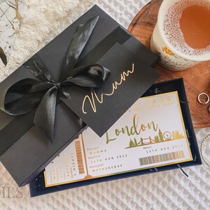 May include: A black gift box with a gold ribbon and a gold tag that says "Mum". The box is open and inside is a white card with a gold border and the text "London Pass - Happy Mother's Day!" with a gold illustration of the London skyline.
