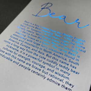 May include: A light gray card with the name "Bear" in blue script. The card provides information about the name's origin and meaning, including its association with strength and courage.