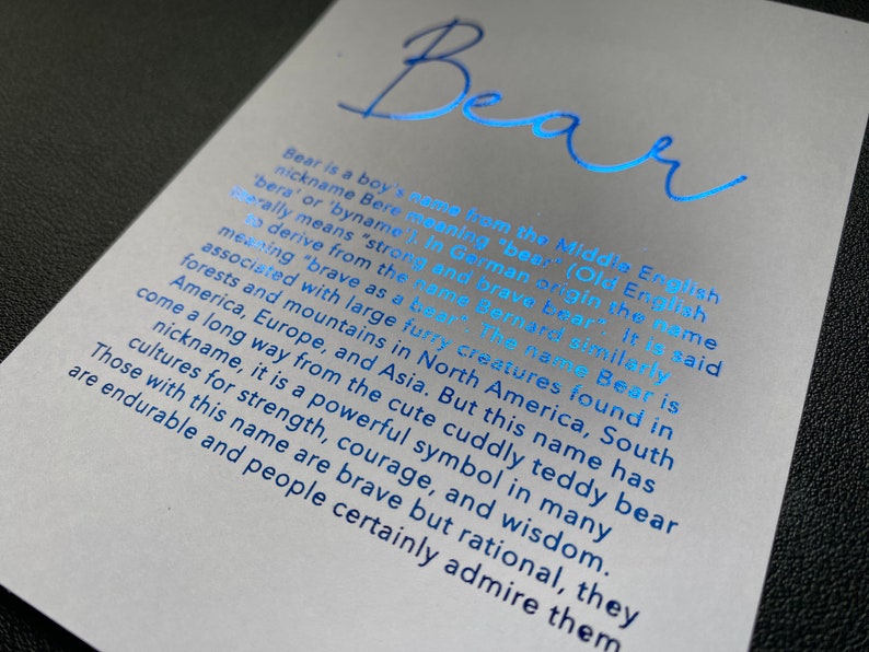 May include: A light gray card with the name "Bear" in blue script. The card provides information about the name's origin and meaning, including its association with strength and courage.