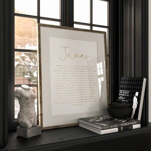May include: A framed print with the name "James" in gold script, displayed on a black shelf with decorative items. The shelf also holds a small bust, books, and a decorative bowl. The print includes text about the name's origins.