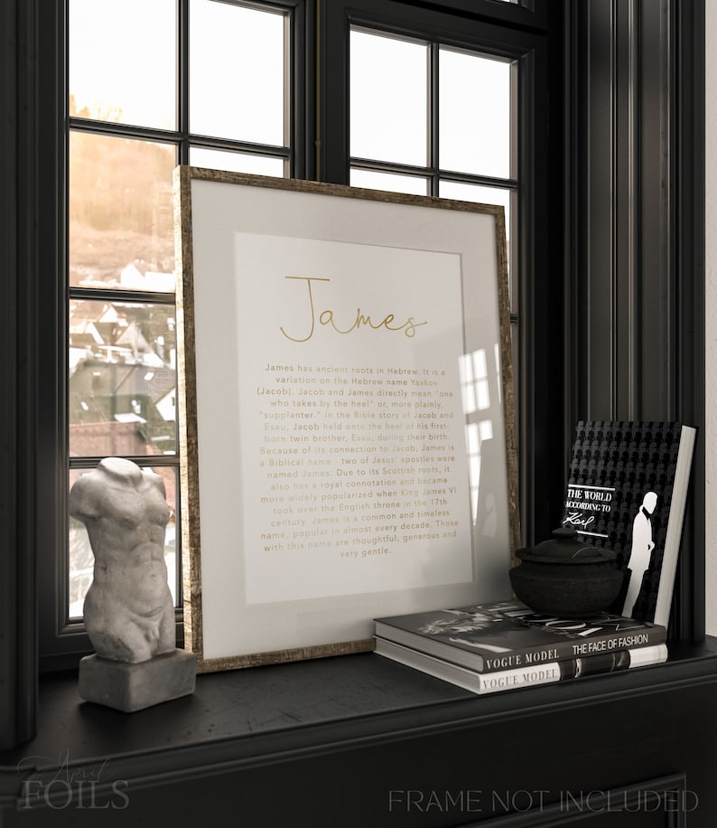 May include: A framed print with the name "James" in gold script, displayed on a black shelf with decorative items. The shelf also holds a small bust, books, and a decorative bowl. The print includes text about the name's origins.