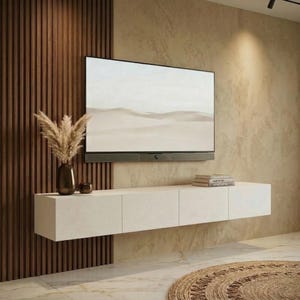 May include: A wall-mounted white floating media console featuring three rectangular storage compartments. The unit is positioned below a flat-screen television and a soundbar, with a dark vase containing dried pampas grass on top.