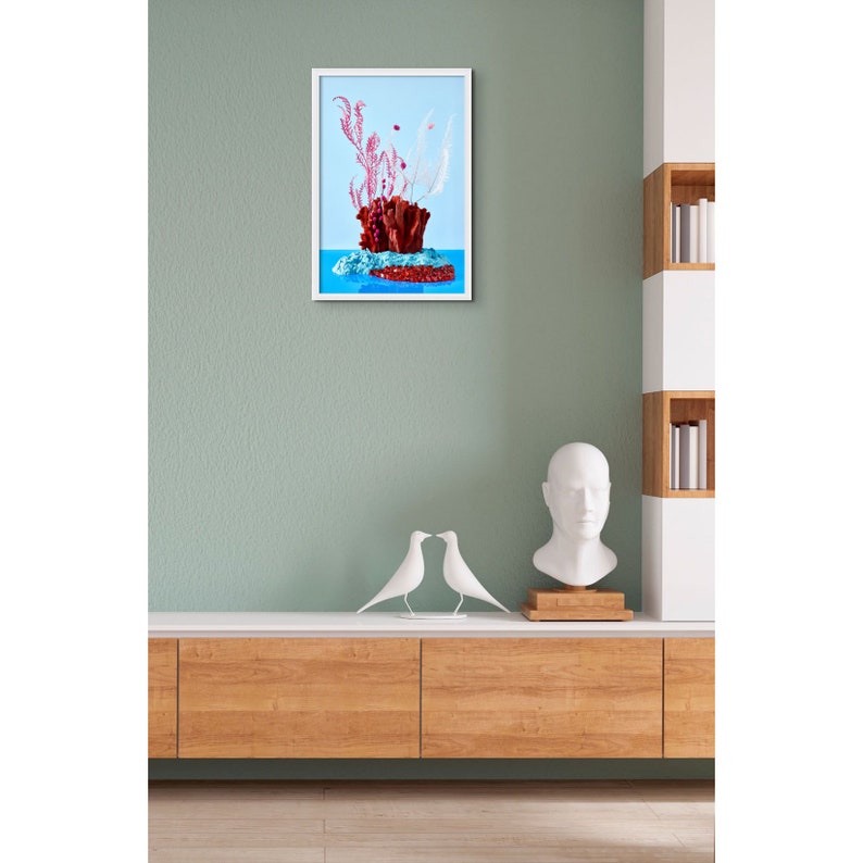 Op de afbeelding: Een ingelijste print van een stilleven met een rood koraalachtig object met roze en witte veren op een blauwe achtergrond.