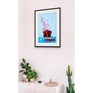 Op de afbeelding: Een ingelijst afdruk van een stilleven met een rood koraalachtig object met roze en witte veren op een blauwe achtergrond.