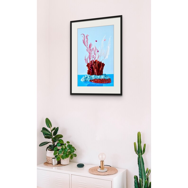 Op de afbeelding: Een ingelijst afdruk van een stilleven met een rood koraalachtig object met roze en witte veren op een blauwe achtergrond.