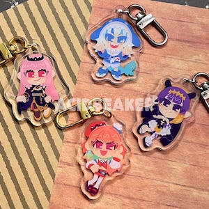 May include: Four acrylic keychains featuring anime-style characters with gold and silver-tone clasps. The characters have pink, blue, purple, and red hair, and are dressed in colorful outfits. The keychains are on a wooden surface.