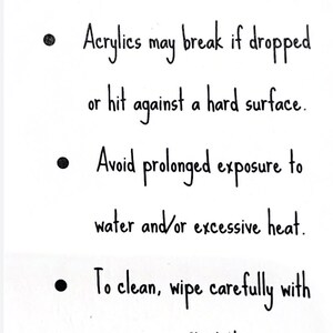 May include: A white background with black handwritten text detailing care instructions. The text advises to handle with care, avoid water and heat, and wipe clean with a soft cloth. It also mentions acrylics may break.