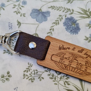 May include: Wooden keyring with a brown leather strap and silver clasp. The wooden tag is engraved with the words "Where it all began" and coordinates. A stylish accessory.