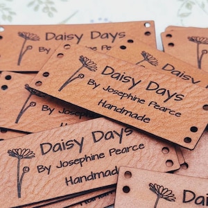 Pu&ograve; includere: Un mucchio di etichette in pelle marrone con il testo "Daisy Days" e "By Josephine Pearce Handmade" stampato su di esse. Ogni etichetta ha un piccolo disegno di margherita.