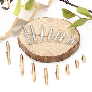 Peut inclure: Assortiment de embouts de tube en métal doré et argenté pour la fabrication de bijoux. Les embouts sont de différentes tailles et sont présentés sur une surface en bois.