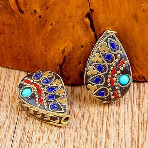 May include: Two teardrop-shaped pendants with intricate blue and red enamel designs and turquoise accents. The pendants are made of brass and have a gold finish.