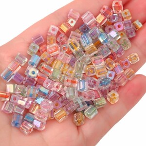 May include: A large assortment of small, iridescent, square-shaped glass beads in various colours, including pink, blue, green, and yellow.