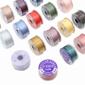 May include: Assortment of 15 spools of thread in various colors, including beige, purple, red, blue, green, yellow, and pink. The spools are labeled "Stitch Yarn FGB 日本製 # 08 made in Japan 50yds".