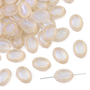 May include: Oval-shaped iridescent beads with a gold-colored border and decorative detailing. The beads are translucent with a pearlescent sheen, and are scattered across a white surface. A needle is inserted through one of the beads.