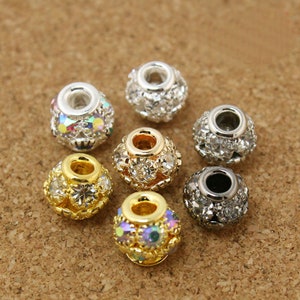 Peut inclure: Assortiment de perles rondes argentées, dorées et noires avec des strass clairs et irisés. Les perles ont un trou au centre pour le perlage.
