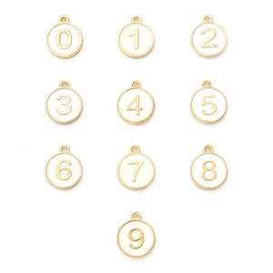 May include: Nine gold-colored metal charms, each featuring a different number from 0 to 9. The numbers are in a gold color, set against a white background within a circular frame. Each charm has a small loop at the top.