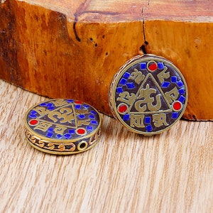 May include: Two round, gold-coloured pendants with blue and red enamel designs. The pendants feature intricate patterns and symbols, including a triangle with a stylised figure inside.