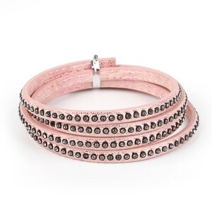 May include: A pink leather bracelet with four rows of rhinestones. The bracelet is made of a soft, flexible leather and has a simple, elegant design.