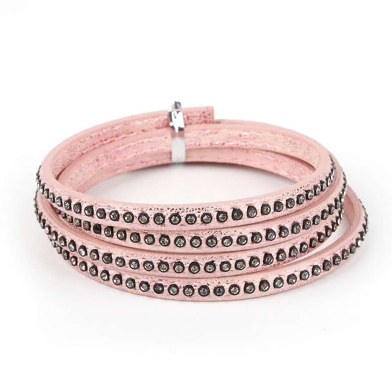 May include: A pink leather bracelet with four rows of rhinestones. The bracelet is made of a soft, flexible leather and has a simple, elegant design.