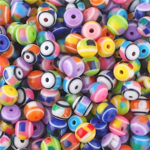 Puede incluir: Una colección de cuentas redondas de plástico de colores con patrones geométricos. Las cuentas tienen un diámetro aproximado de 1 cm y están disponibles en una variedad de colores, incluyendo rojo, azul, verde, amarillo, naranja, morado y blanco.