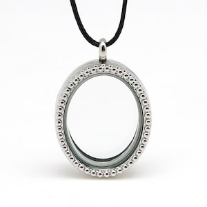 Puede incluir: Un medallón ovalado de plata con un borde de cuentas y un collar de cordón negro.