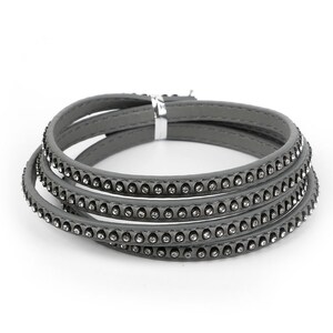 May include: A gray leather bracelet with a row of rhinestones around the edge. The bracelet is made of multiple layers of leather.