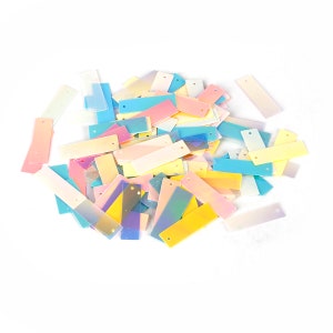 May include: A pile of iridescent rectangular sequins in various pastel colors, including pink, blue, yellow, and green.
