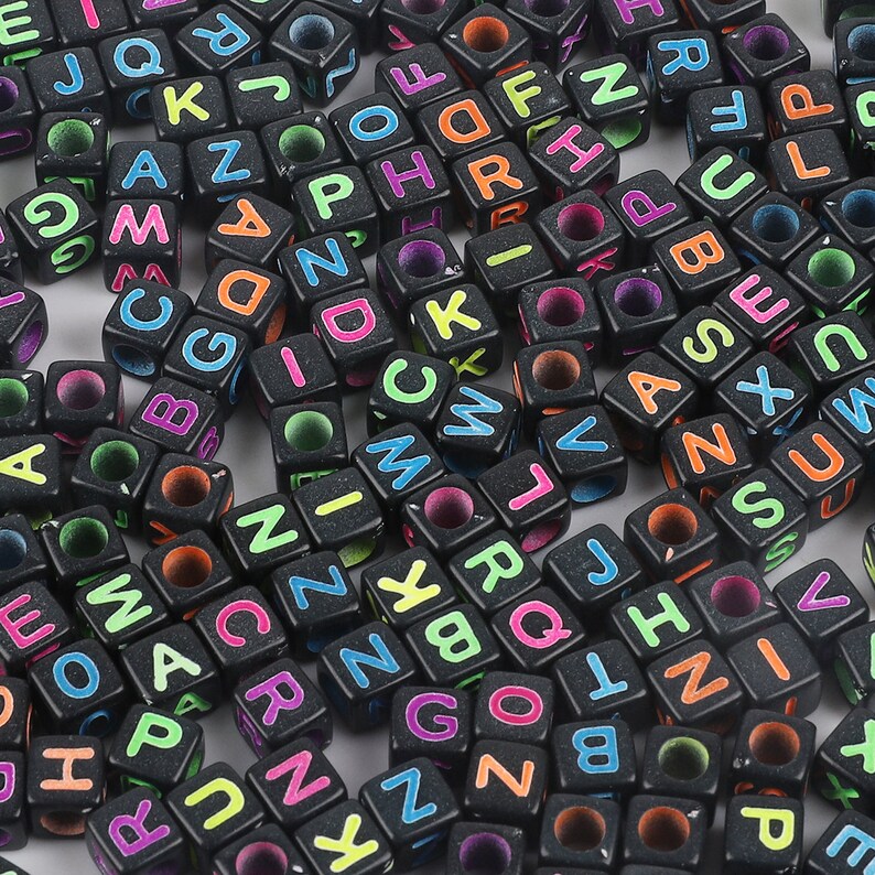 May include: A large pile of black letter beads with colorful neon letters. The beads are cube shaped and have a hole in the center.