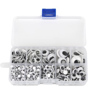 Può includere: Una scatola di plastica trasparente piena di occhietti bianchi di varie dimensioni con pupille nere. La scatola ha otto scomparti e un coperchio blu.