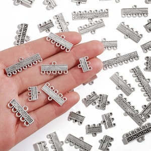 May include: A collection of silver-toned metal connector charms with a decorative wave pattern. The charms have four loops for attaching jewellery pieces.