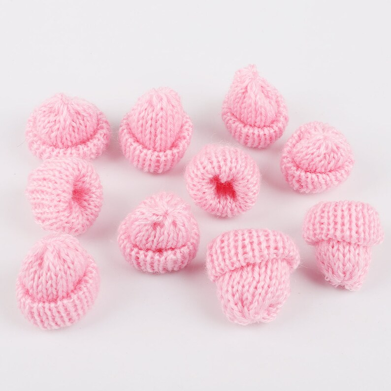 May include: A collection of ten pink knitted miniature hats. The hats are small and have a classic beanie shape.