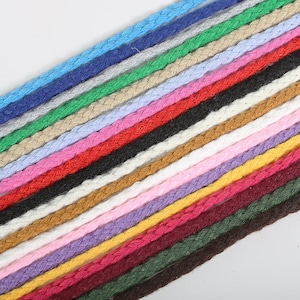 May include: A collection of 24 different colored braided cords. The cords are arranged in a diagonal line, with the lightest colors at the top and the darkest colors at the bottom.