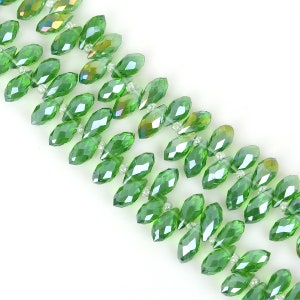 May include: A strand of green faceted glass beads with iridescent accents. The beads are shaped like teardrops and are strung on a clear thread.