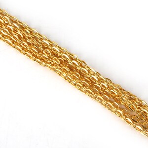 May include: A close-up of a gold chain, showing the individual links. The chain is lying flat on a white surface.