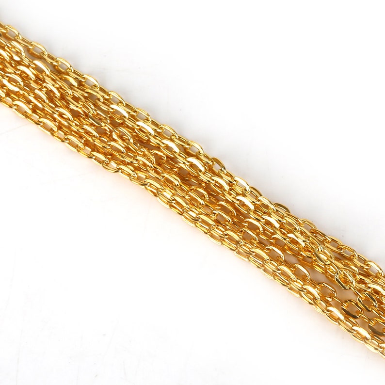 May include: A close-up of a gold chain, showing the individual links. The chain is lying flat on a white surface.