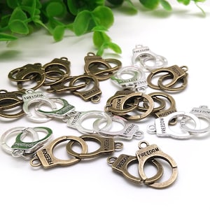 May include: A collection of antique silver and bronze-toned metal charms shaped like handcuffs with the word "FREEDOM" engraved on them.