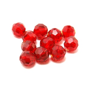 Op de afbeelding: Een groep rode gefacetteerde glazen kralen, verspreid over een witte achtergrond.