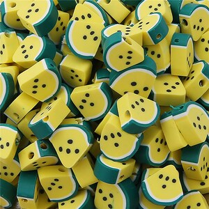 Puede incluir: Un montón grande de cuentas de plástico de color amarillo y verde con forma de sandía. Las cuentas tienen un acabado brillante.