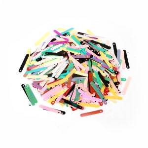 May include: A large pile of colorful, iridescent sequins in the shape of long, thin rectangles. The sequins are scattered on a white background.