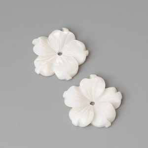 Może przedstawiać: Dwa białe, rzeźbione kształty kwiatów muszli z otworem w środku.