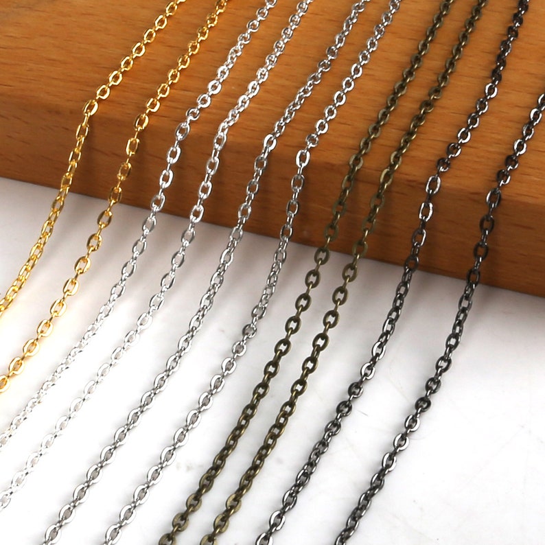 May include: Assortment of chain links in gold, silver, bronze, and black metal. The chains are laid out in a row on a wooden surface.
