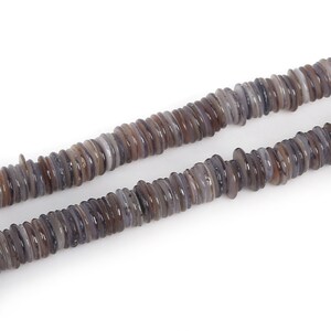Könnte beinhalten: Eine Schnur grauer und brauner Muschelkernperlen. Die Perlen sind flach und rund und auf einer durchsichtigen Schnur aufgefädelt.