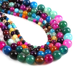 May include: A strand of colourful agate beads in various shades of green, blue, pink, orange, and brown. The beads are round and smooth, and they are arranged in a random pattern.