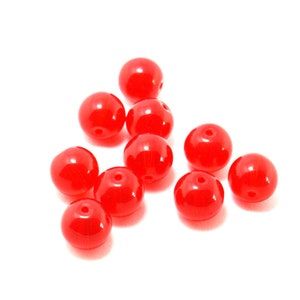 Könnte beinhalten: Zehn leuchtend rote runde Perlen aus Glas. Die Perlen sind glatt und glänzend.